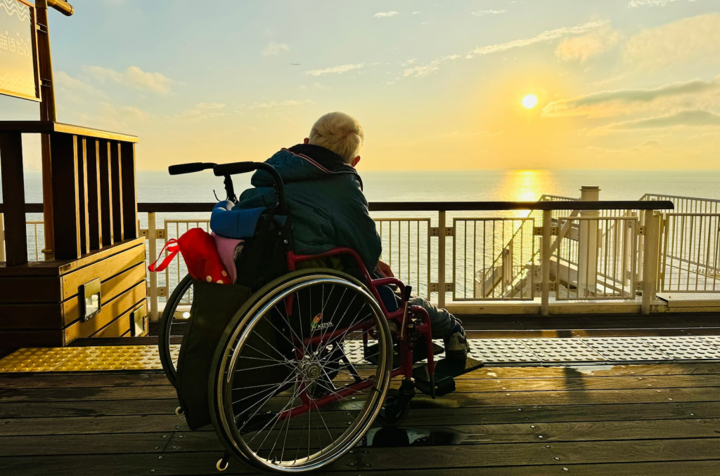 夕日が沈む海を眺める車いす利用者の方