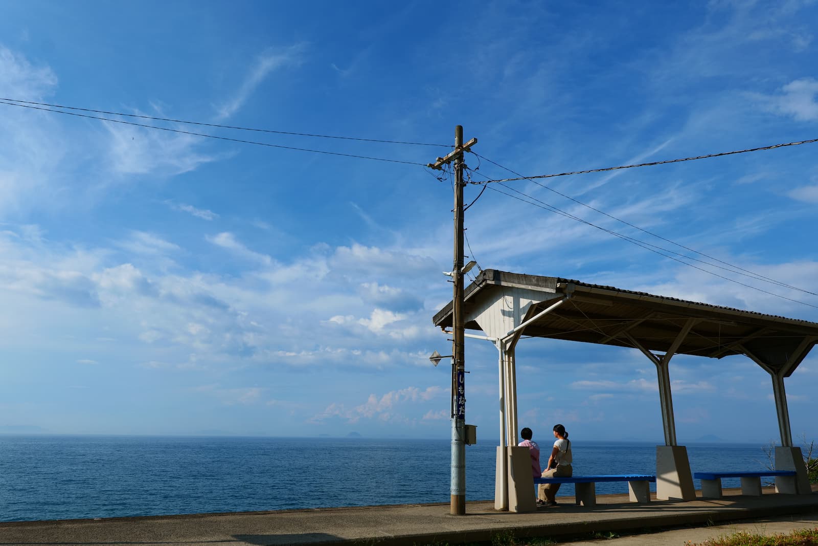 海が見える小さな駅で夫婦が電車を待つ様子