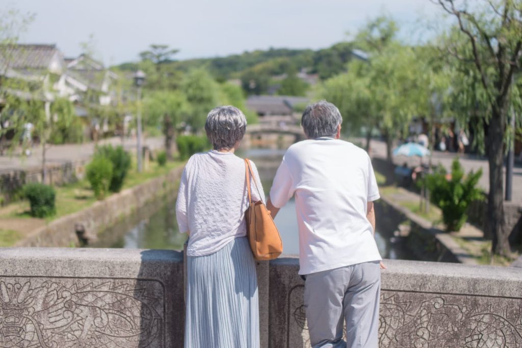 高齢夫婦が橋の上で情緒あふれる川沿いの街を見る旅の様子