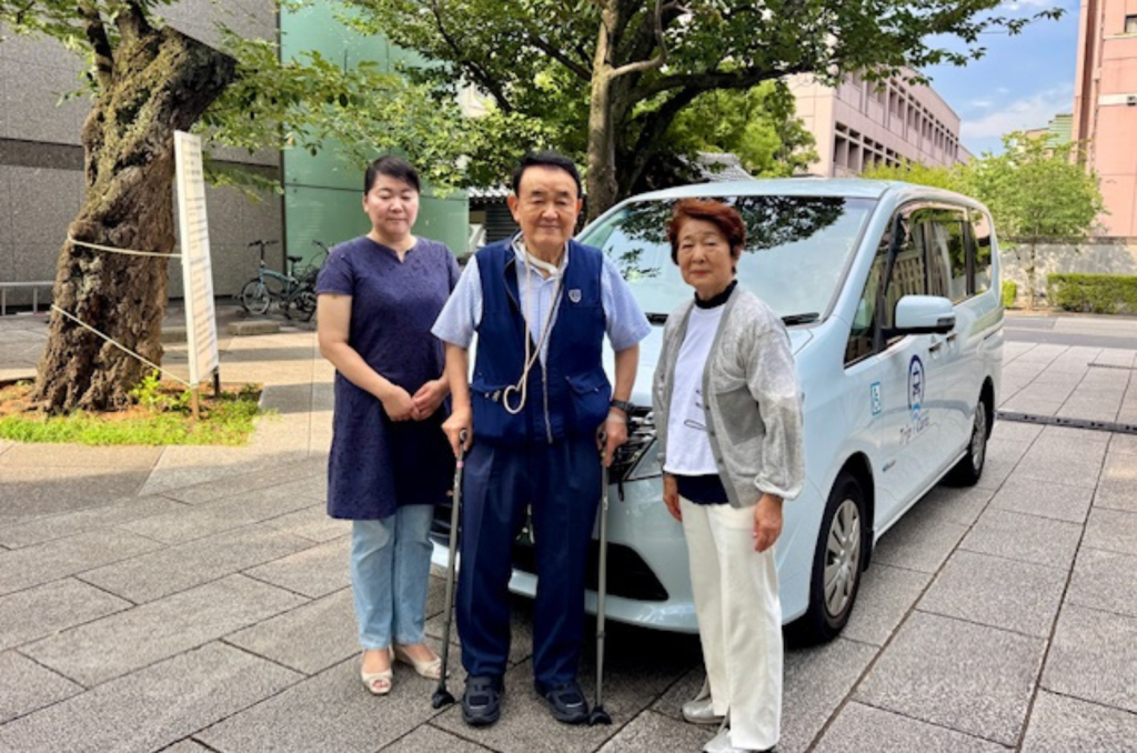 福祉介護タクシー車両と日帰り旅行を楽しむ高齢者夫婦と娘