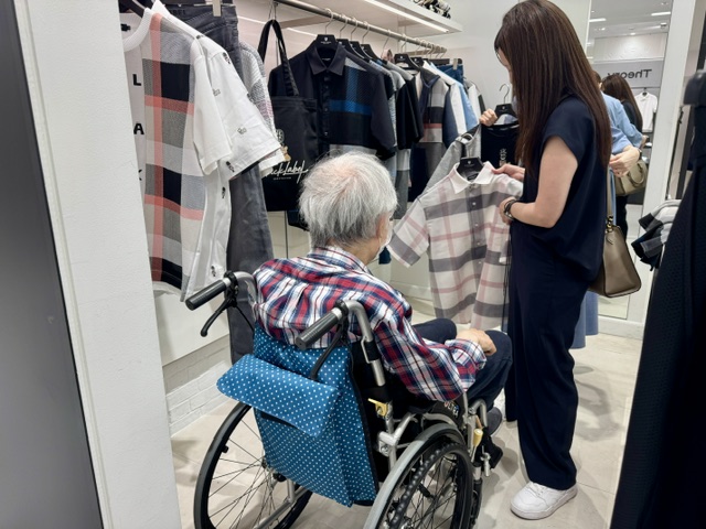 小田急デパートのブラックレーベルで洋服を選ぶ車いすの高齢者と家族